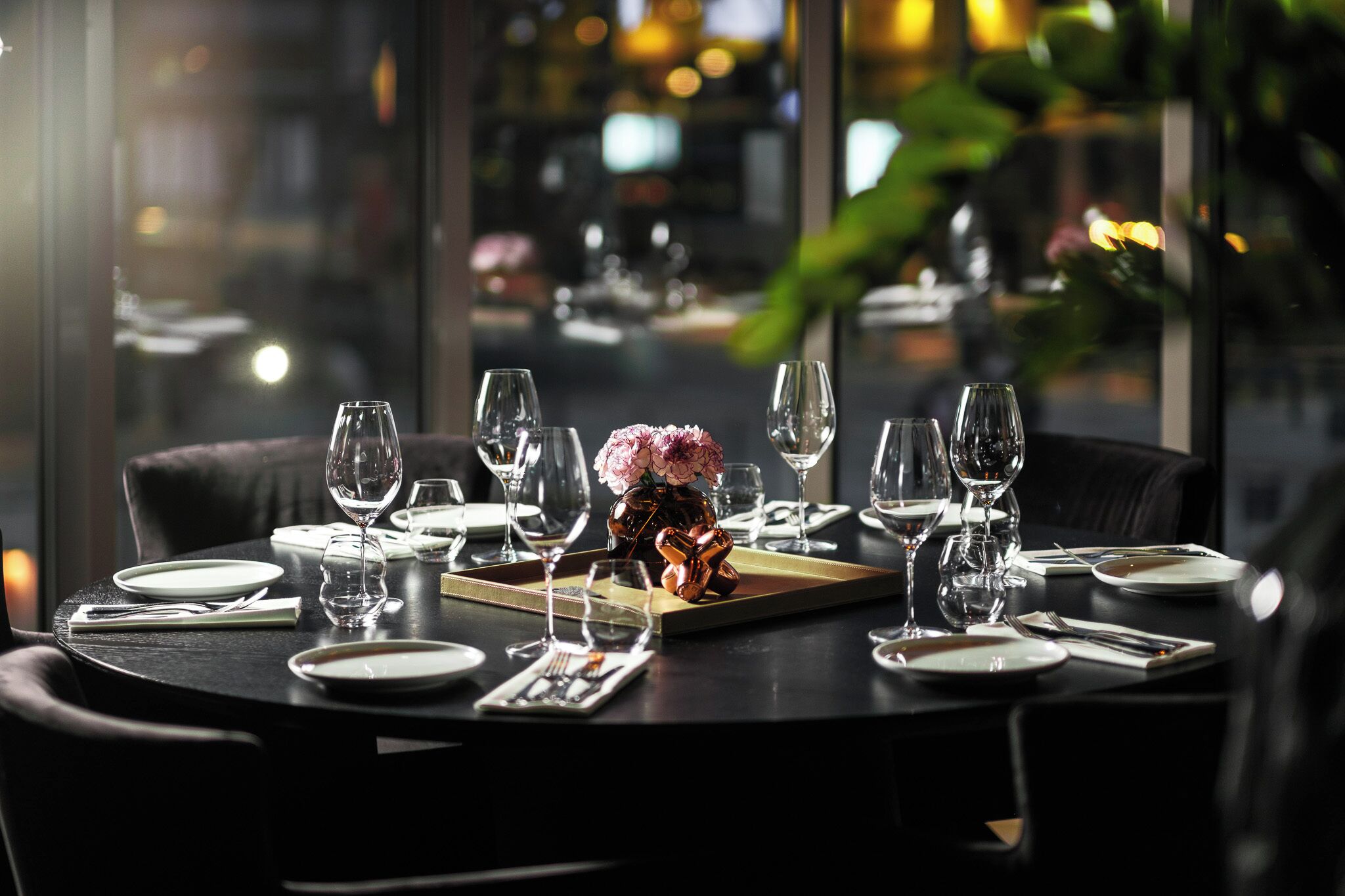 Une table à manger dressée pour un repas, avec plusieurs verres à vin, des assiettes et un centre de table.