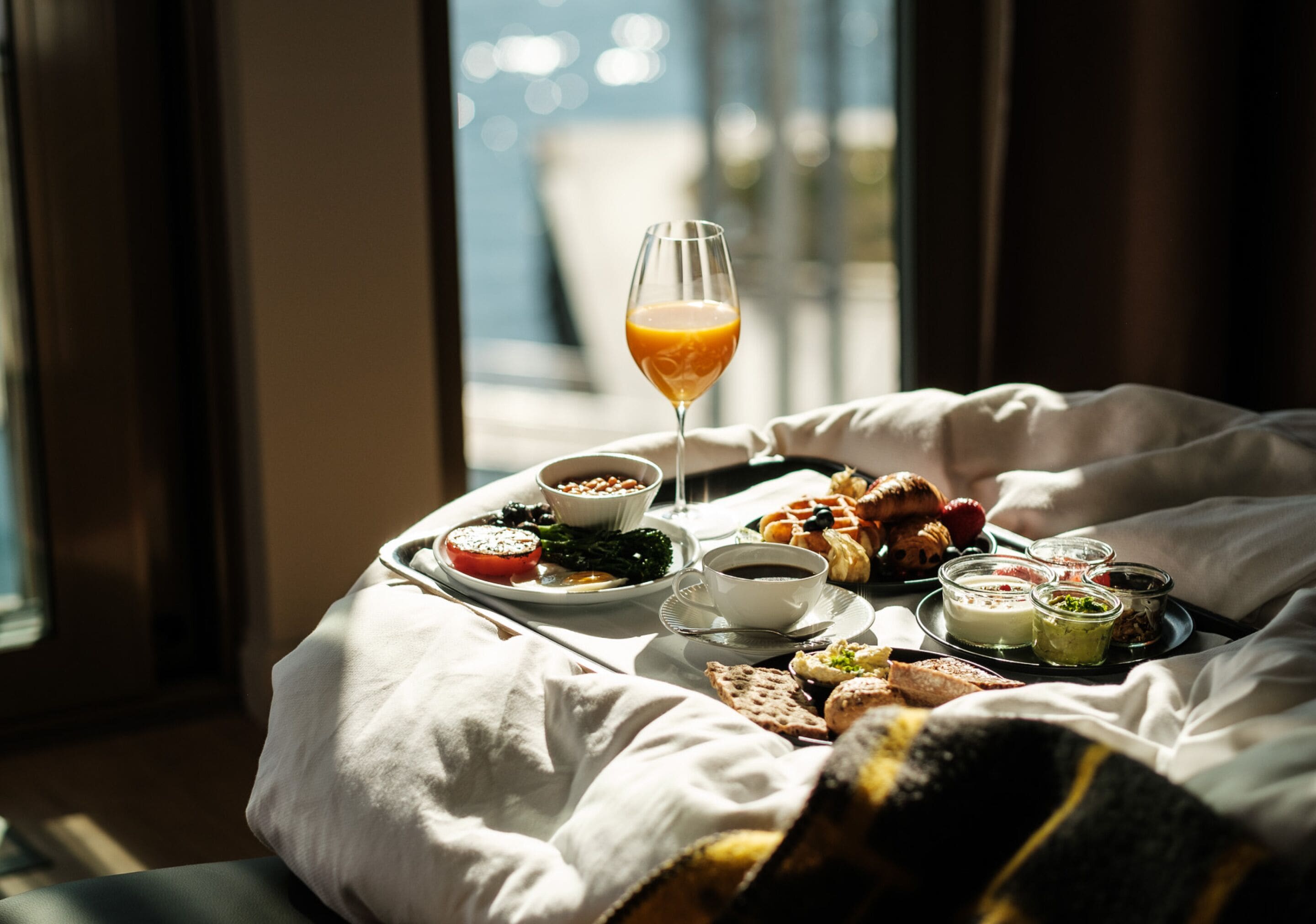 A breakfast tray with various foods and drinks on a bed.