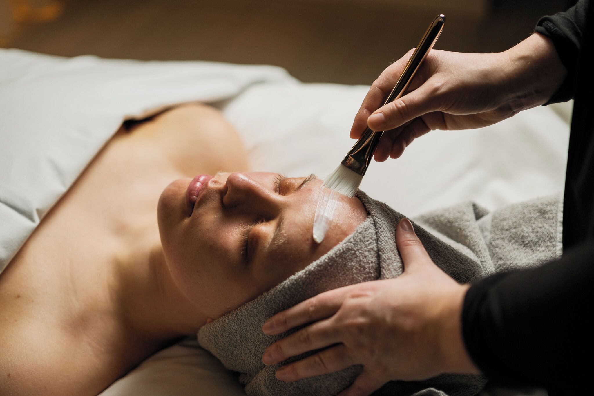 Una persona estesa amb una tovallola al coll, rebent un tractament facial.