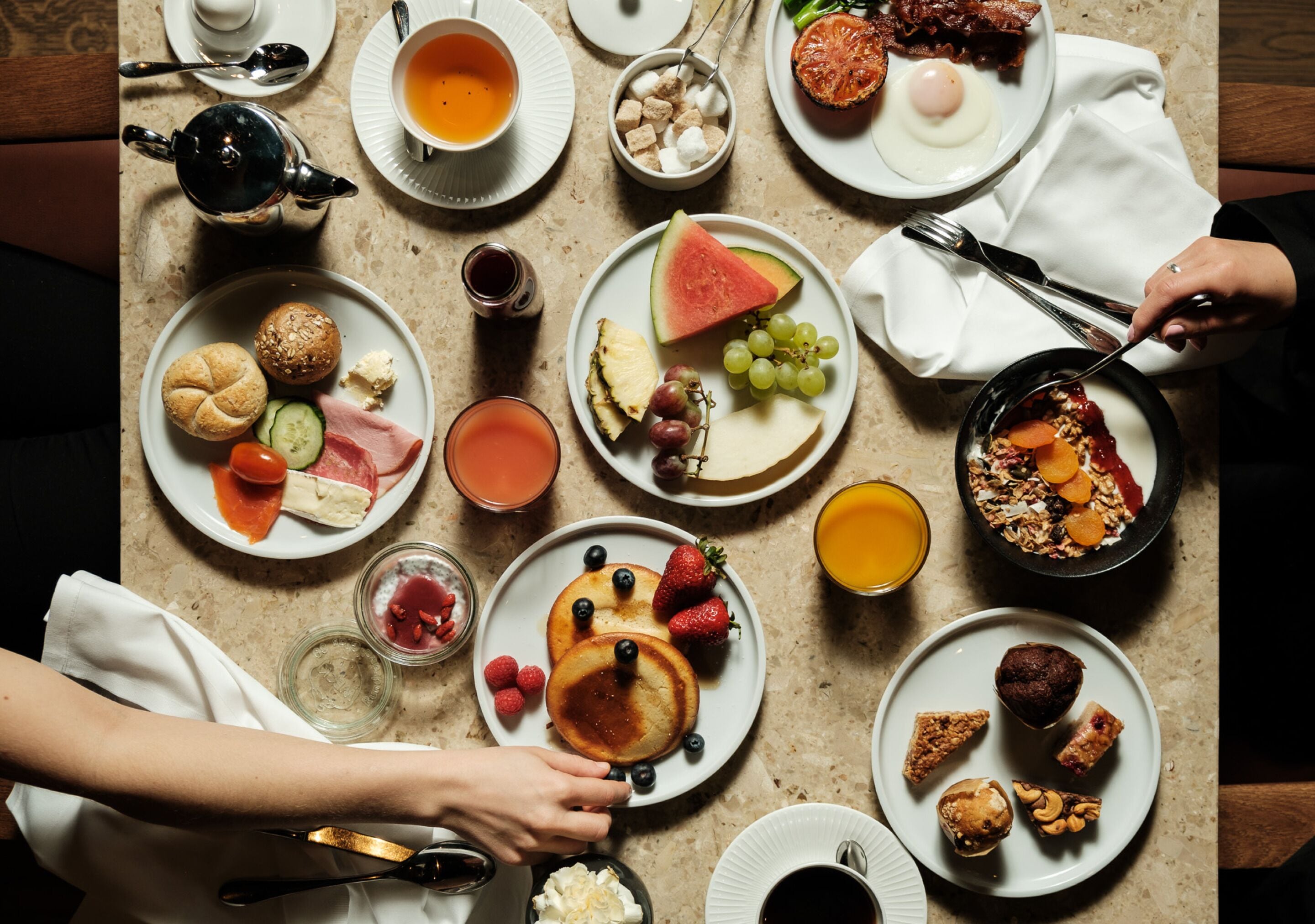 A breakfast setting with various dishes including pancakes, fruits, and beverages on a table.