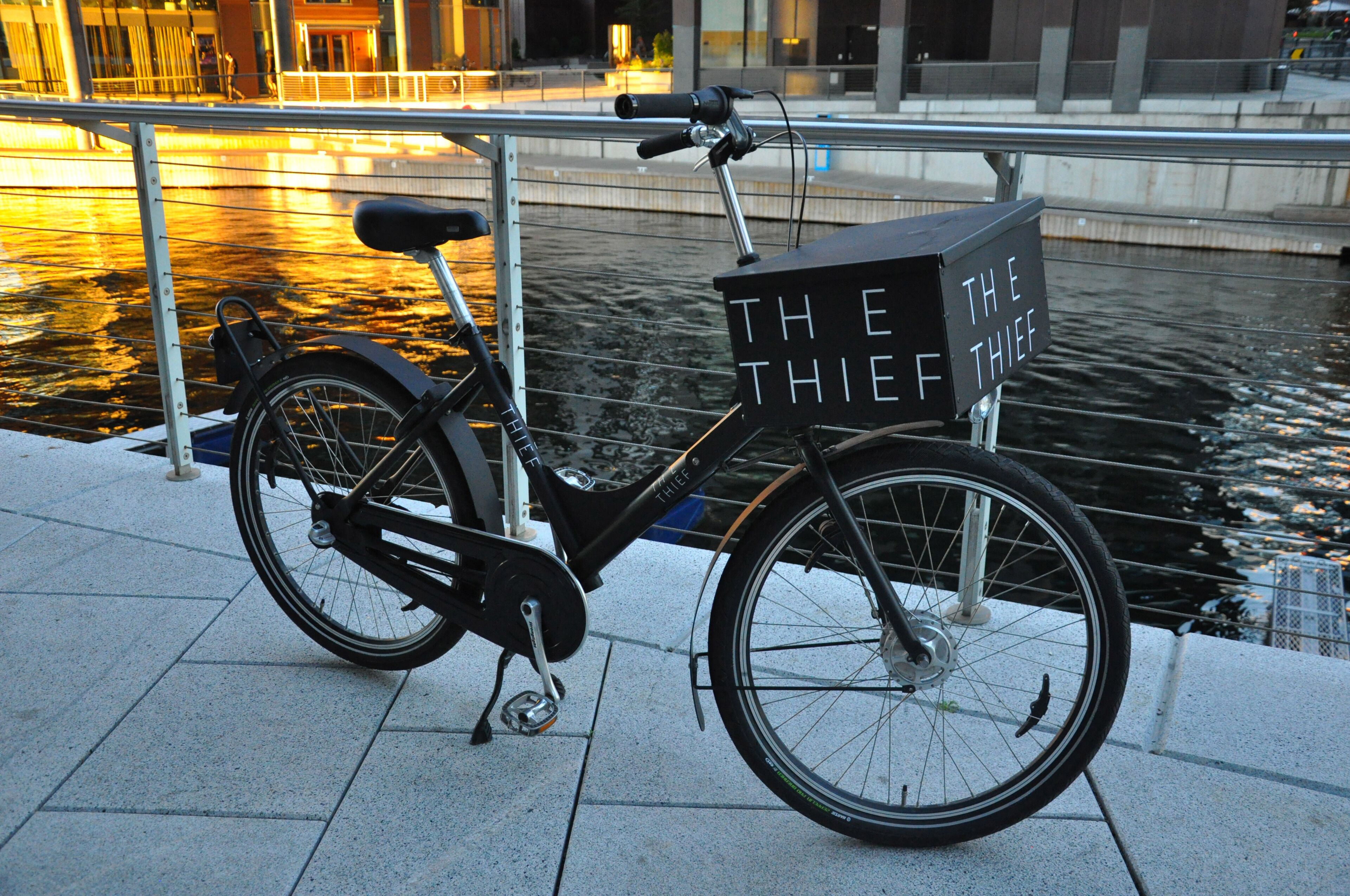 Una bicicleta estática con una canasta que dice 'THE THIEF' estacionada junto a un canal.