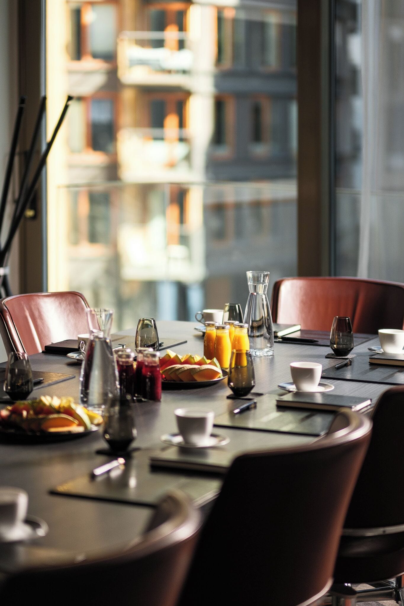 Una mesa de comedor dispuesta con diferentes vasos, una jarra y platos, con vista a un edificio a través de la ventana.