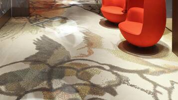 Un vestíbulo moderno con alfombra estampada, techo decorativo y dos sillones naranjas.