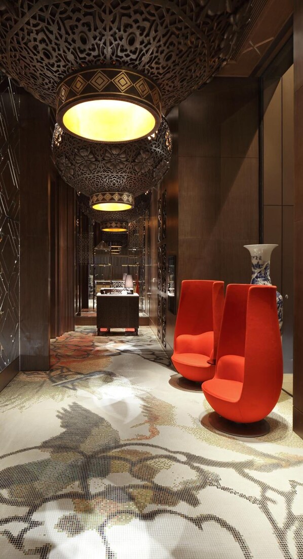 A modern lobby with a patterned carpet, a decorative ceiling, and two orange chairs.