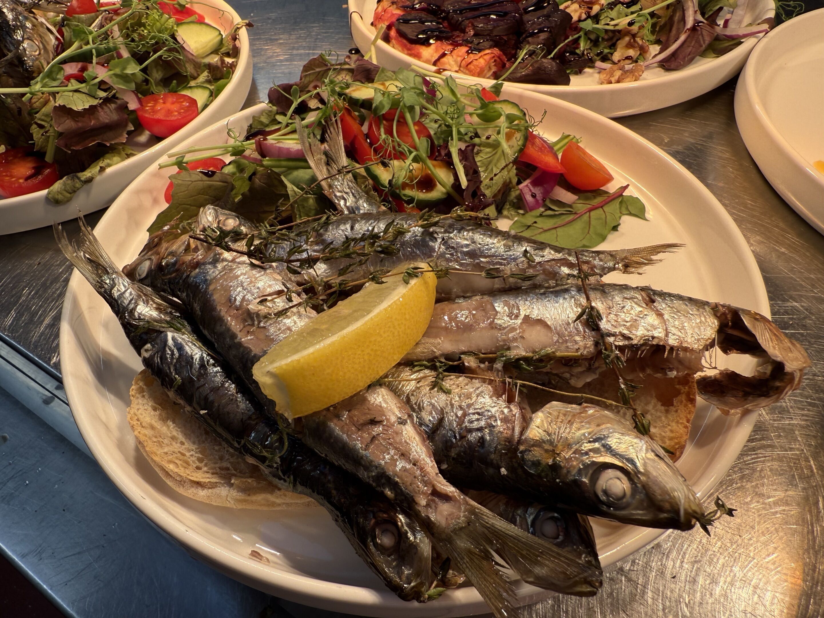 A plate of grilled fish with lemon and herbs, accompanied by various salads.