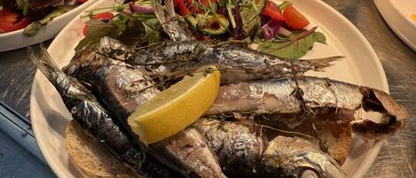 A plate of grilled fish with lemon and herbs, accompanied by various salads.