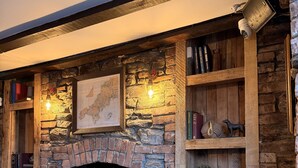 A rustic interior with a stone fireplace, wooden shelves, and a map on the wall. - The Black Swan (Helston)