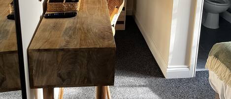 Una habitación con una mesa de madera, un espejo, una cesta, un control remoto y un armario.