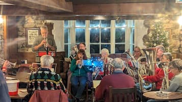 A group of people seated in a room with a stone wall and wooden beams, engaged in a musical performance.