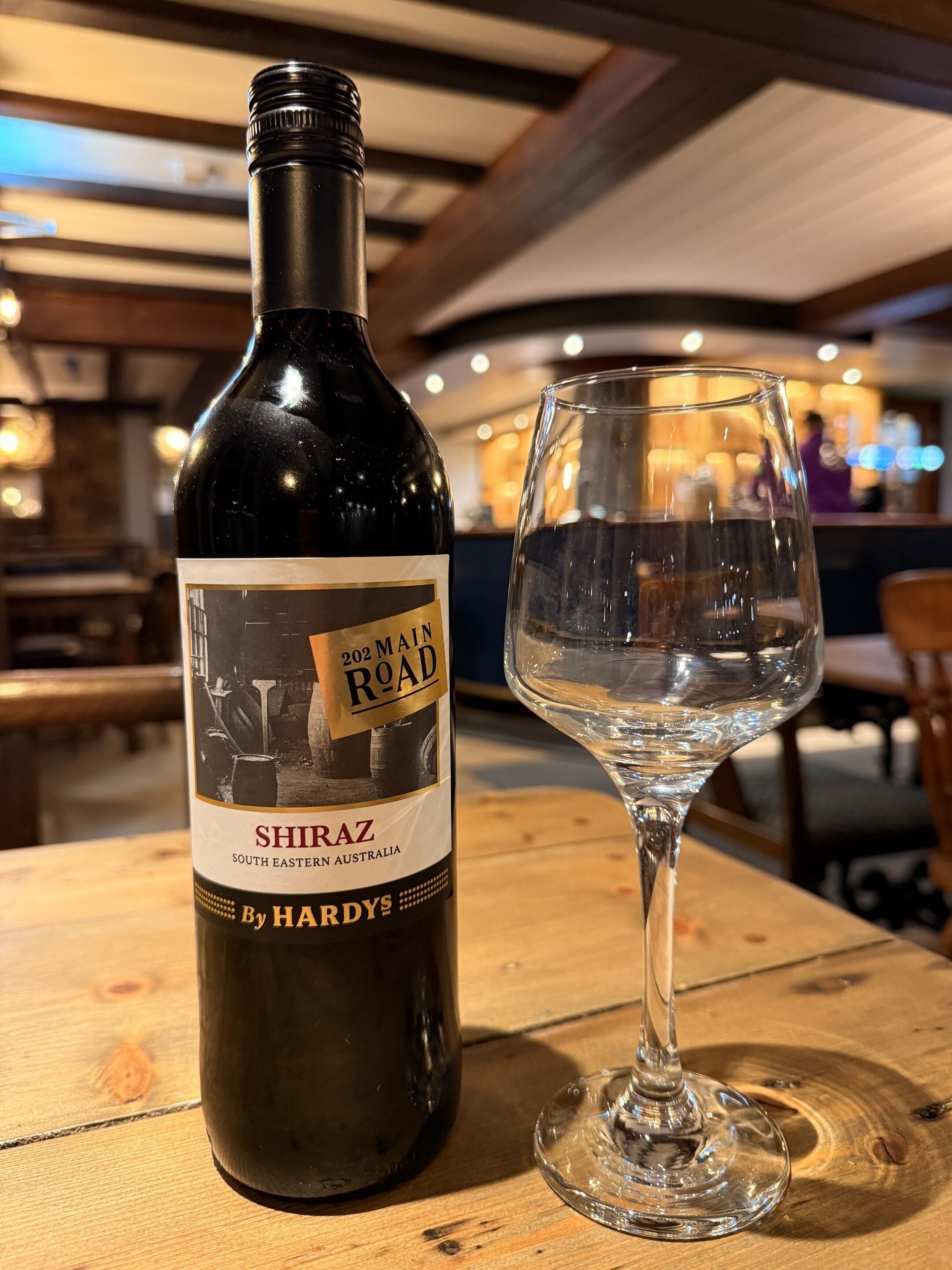 A bottle of Shiraz wine and an empty wine glass on a wooden table in a restaurant.