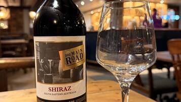 A bottle of Shiraz wine and an empty wine glass on a wooden table in a restaurant.