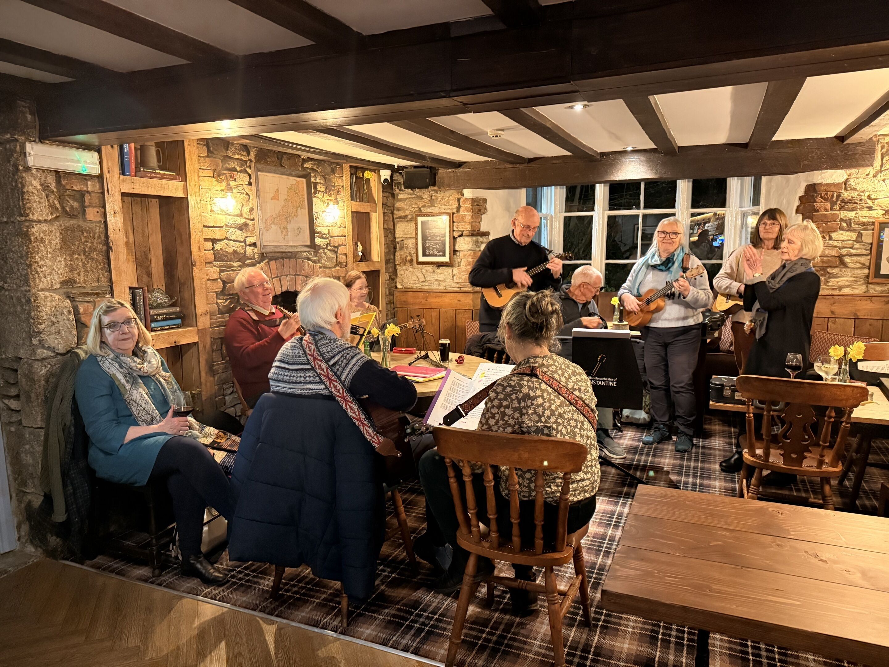 A group of people in a rustic room with stone walls, wooden beams, and a fireplace.