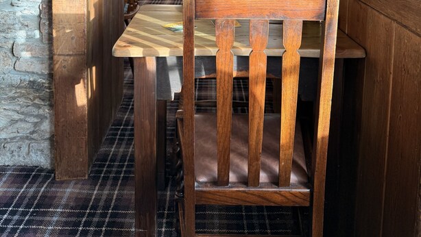 A wooden interior with a stone wall, a wooden table, and a chair. - The Black Swan (Helston)