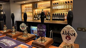 A bar area with multiple beer taps, a display of wine bottles, and a television screen. - The Black Swan (Helston)