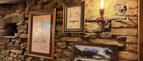 Un mur en pierre orné d’illustrations maritimes encadrées et d’une image représentant un paysage côtier.