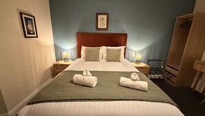 A hotel room with a large bed, two bedside tables with lamps, a wardrobe, and a framed picture on the wall. - The Black Swan (Helston)