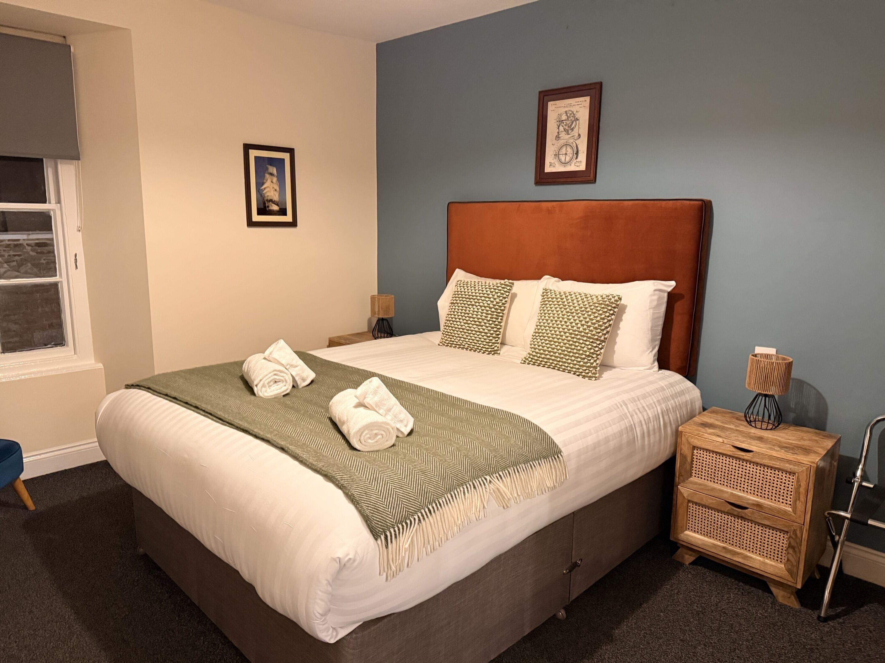 A neatly made bed with a green throw, a wooden headboard, and a nightstand with a lamp.