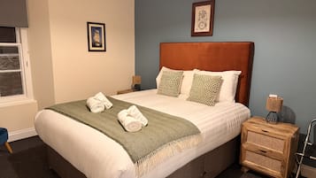 A neatly made bed with a green throw, a wooden headboard, and a nightstand with a lamp.