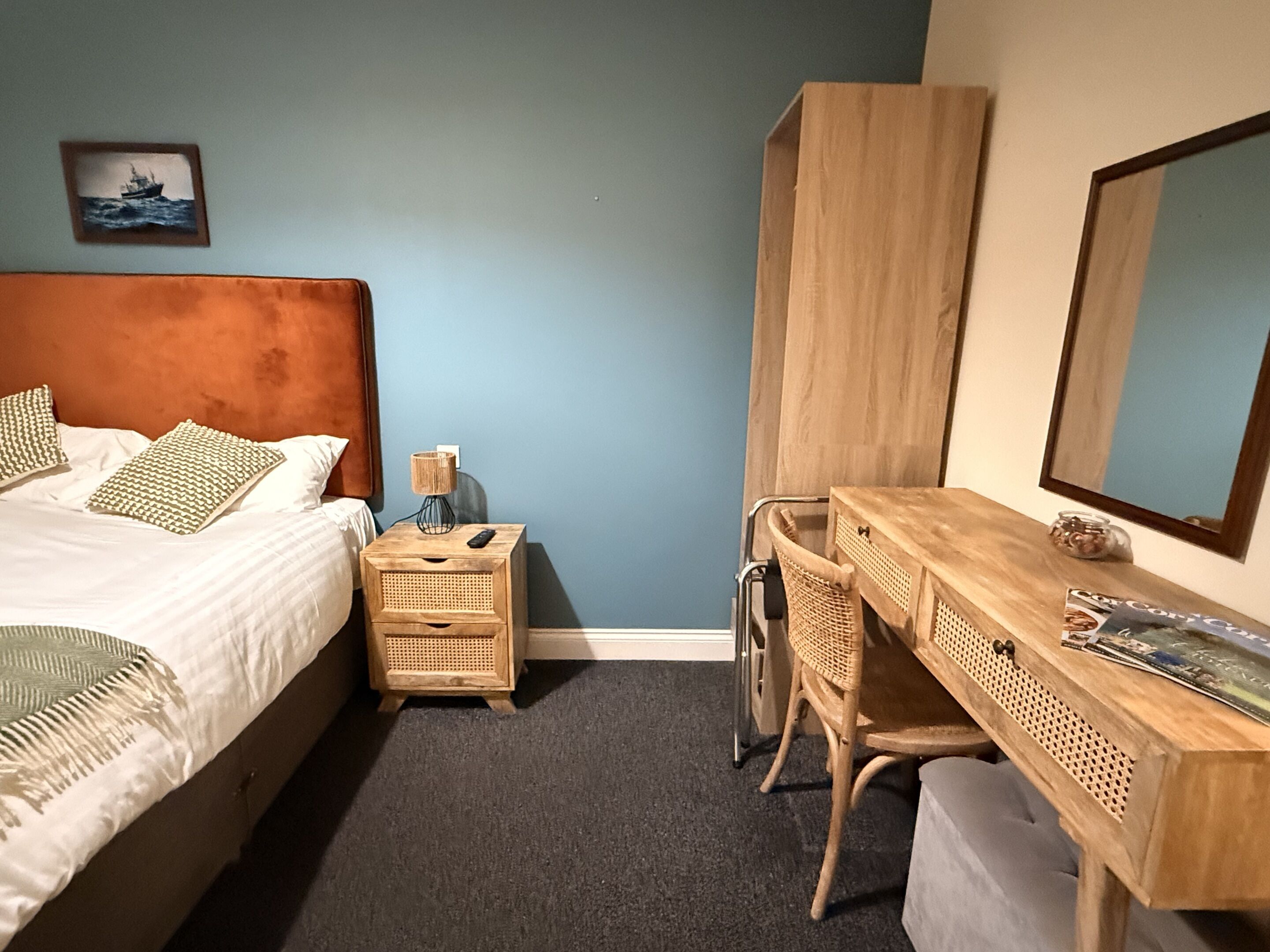 Un dormitorio con cama, mesita de noche, lámpara, escritorio, silla y un espejo grande.