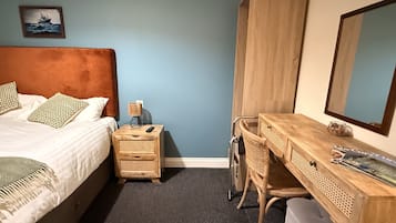 Un dormitorio con cama, mesita de noche, lámpara, escritorio, silla y un espejo grande.