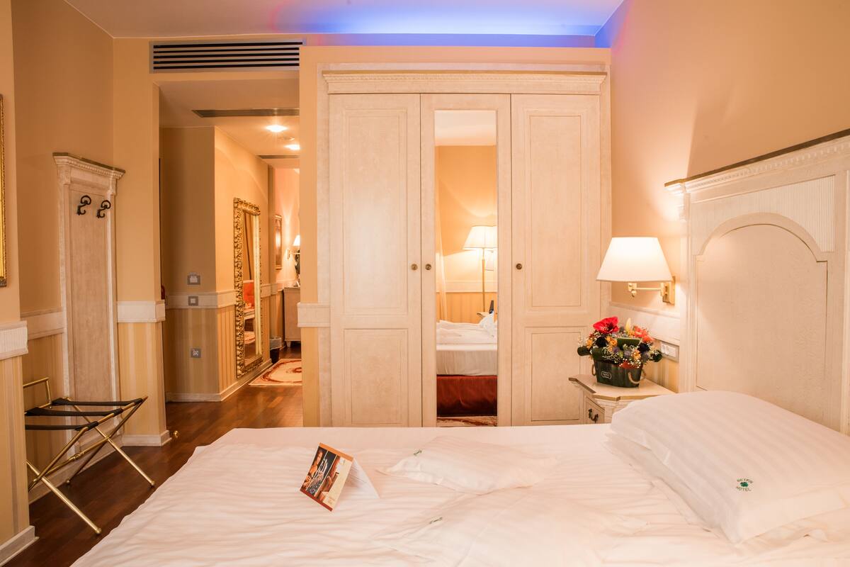 A hotel room with a large bed, a wardrobe, a bedside table with a lamp, and a mirror.