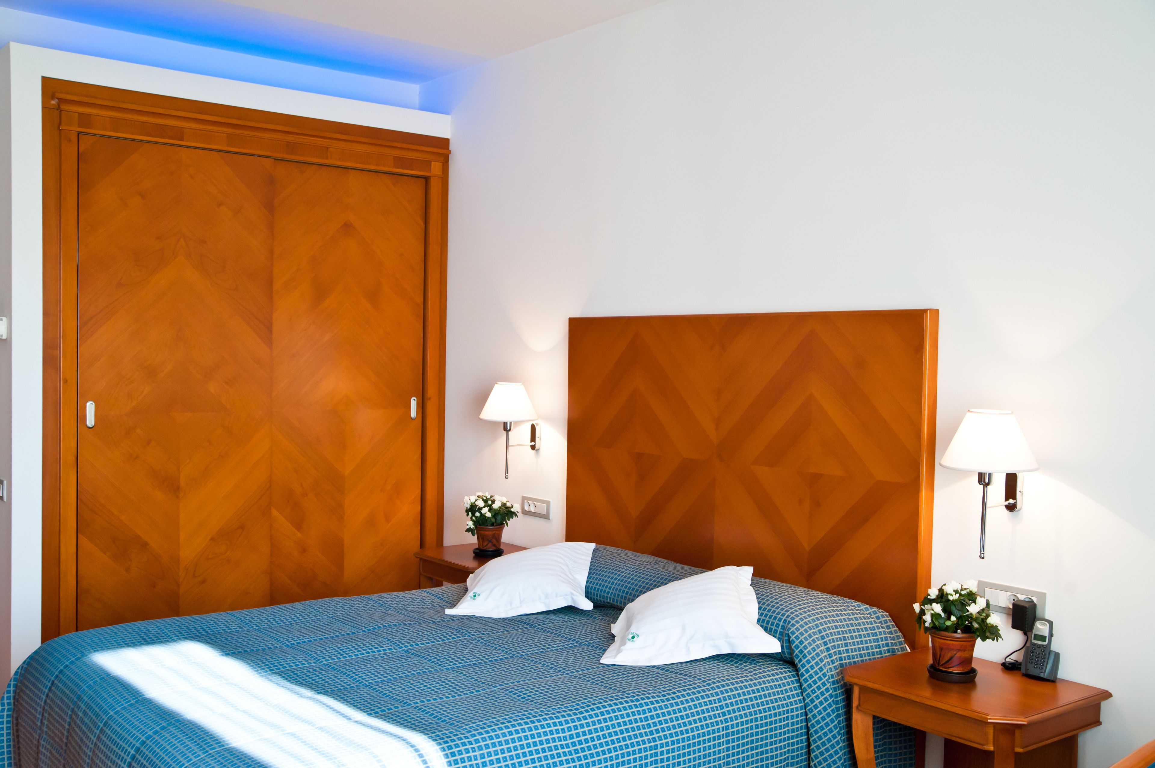 A hotel room with a large bed, two bedside tables, a wooden headboard, and a wooden wardrobe.