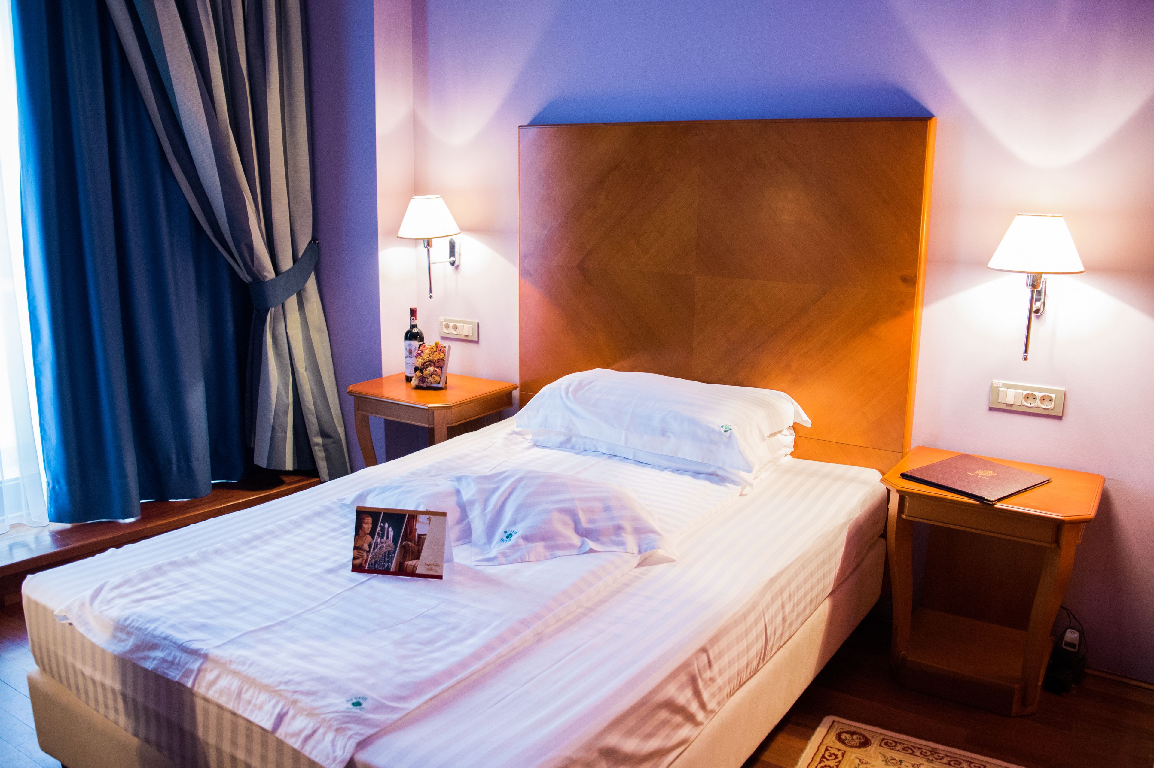 A neatly made bed with a pillow, a bedside table with a lamp, and a small table with a laptop.