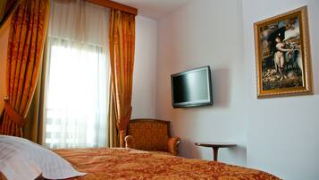 A hotel room with a bed, a chair, a small table, a TV, and a painting on the wall.