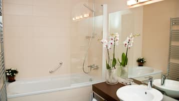 A modern bathroom with a bathtub, two sinks, a glass shower enclosure, and decorative orchids.