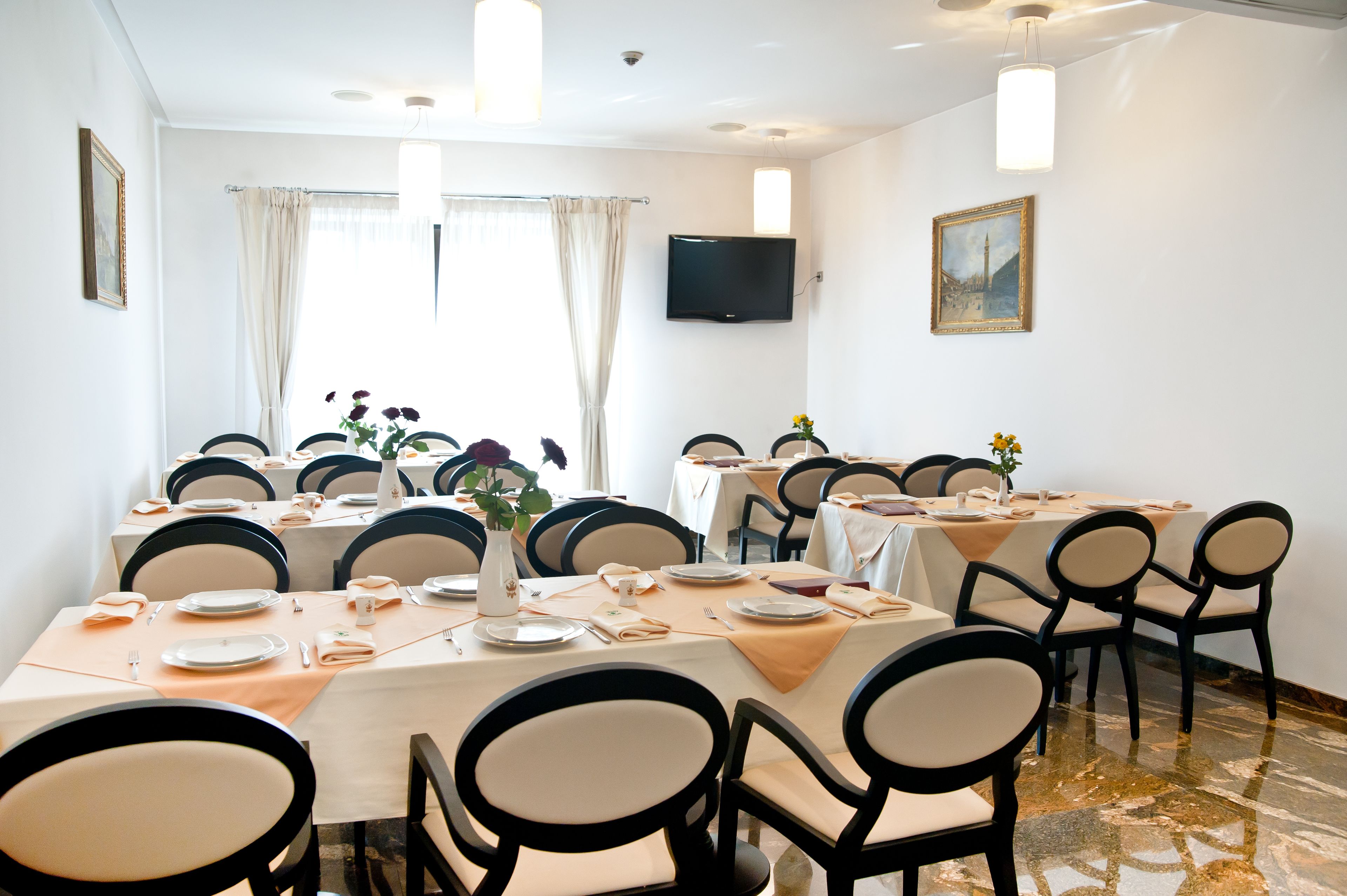A dining area with multiple tables set for meals, chairs, a flat-screen TV, and artwork on the walls.