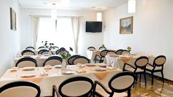 A dining area with multiple tables set for meals, chairs, a flat-screen TV, and artwork on the walls.