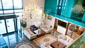 A spacious lobby with a large chandelier, multiple seating areas, and a glass railing overlooking a lower level. - Hotel Beyfin (Cluj-Napoca)