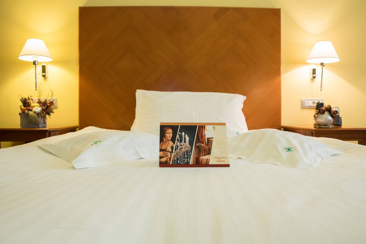 A hotel room with a large bed, two bedside lamps, a wooden headboard, and a decorative item on the nightstand.