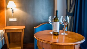 A wooden table with a bottle of wine and two glasses, a lamp, and a blue chair in a hotel room. - Hotel Beyfin (Cluj-Napoca)