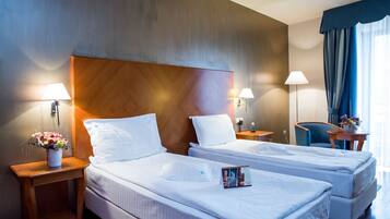 A hotel room with two beds, a wooden headboard, bedside lamps, a small table with a vase of flowers, and a chair.