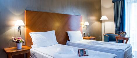 A hotel room with two beds, a wooden headboard, bedside lamps, a small table with a vase of flowers, and a chair.