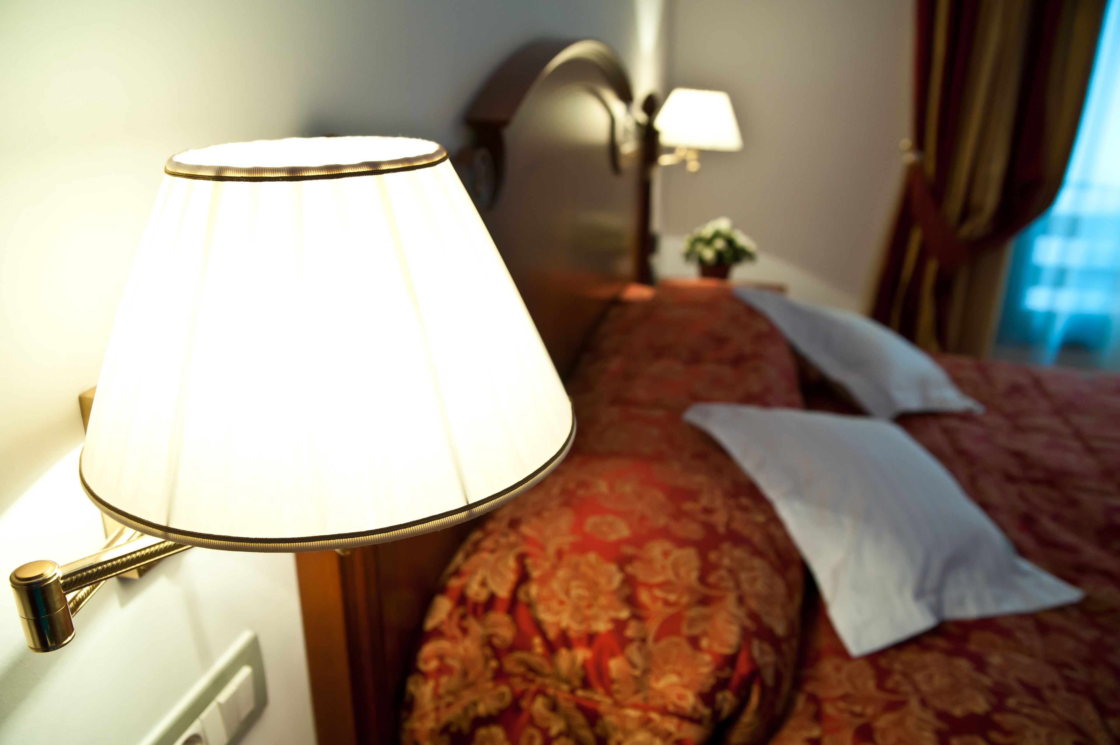 A hotel room with a bed, a bedside lamp, and a nightstand with a lamp.