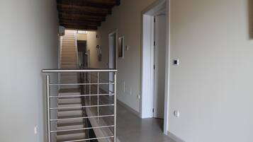 Un pasillo con escalera de metal, techo de madera y una puerta blanca al final.