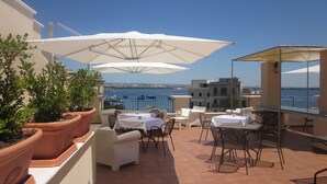 Una terraza con mobiliario exterior, plantas en macetas y vista al mar.