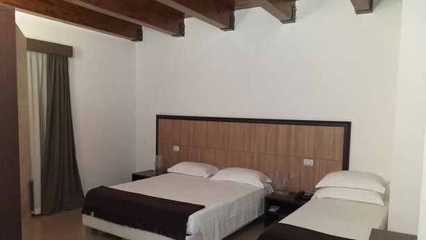Habitación de hotel con dos camas, cabeceros de madera y un ventanal con cortinas.