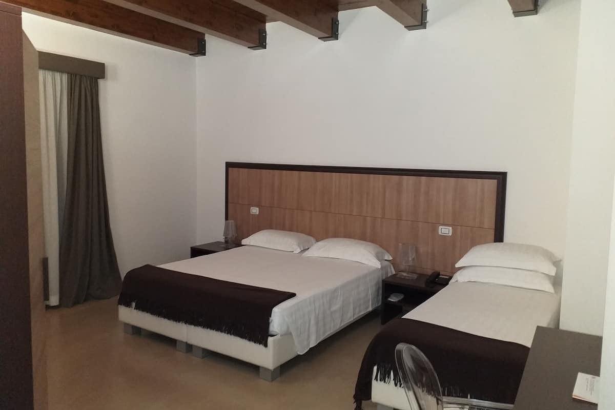 Habitación de hotel con dos camas, cabeceros de madera y un ventanal con cortinas.