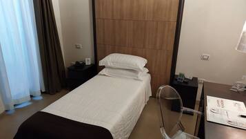 A hotel room with a bed, a desk with a chair, a nightstand, and a wardrobe.