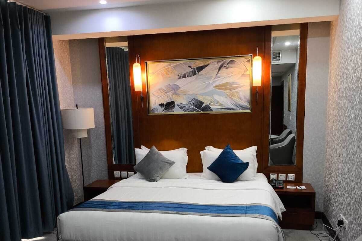 Quarto de hotel com cama, mesa de cabeceira, abajur e um quadro na parede.