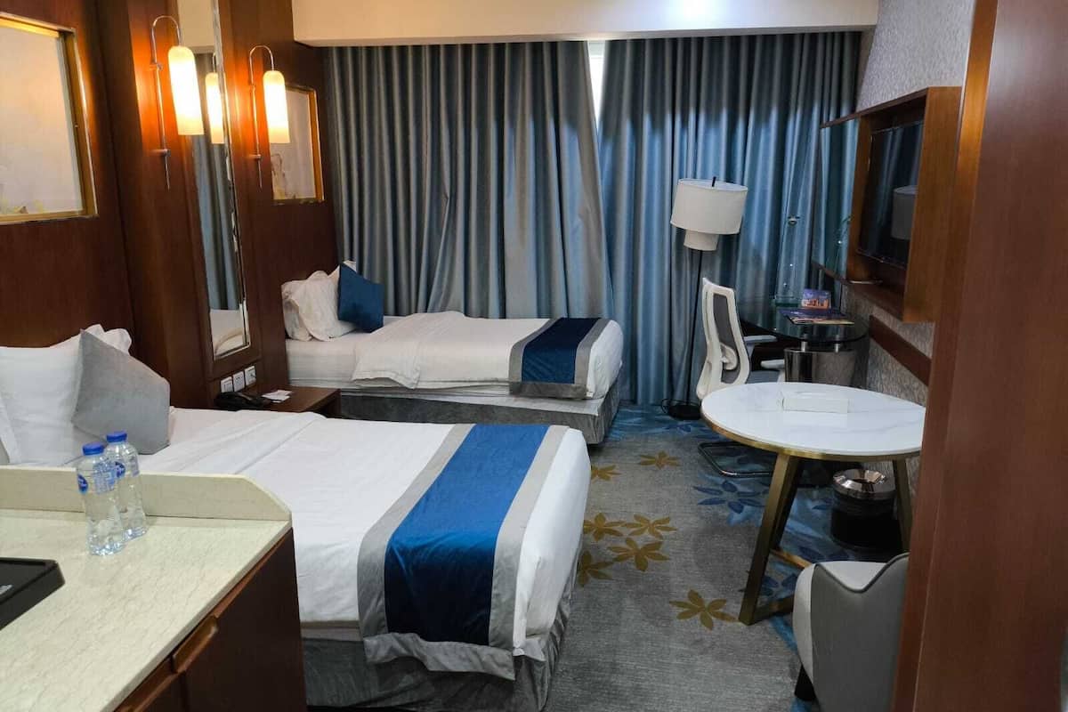 Quarto de hotel com duas camas, uma escrivaninha, uma cadeira, uma televisão e banheiro.