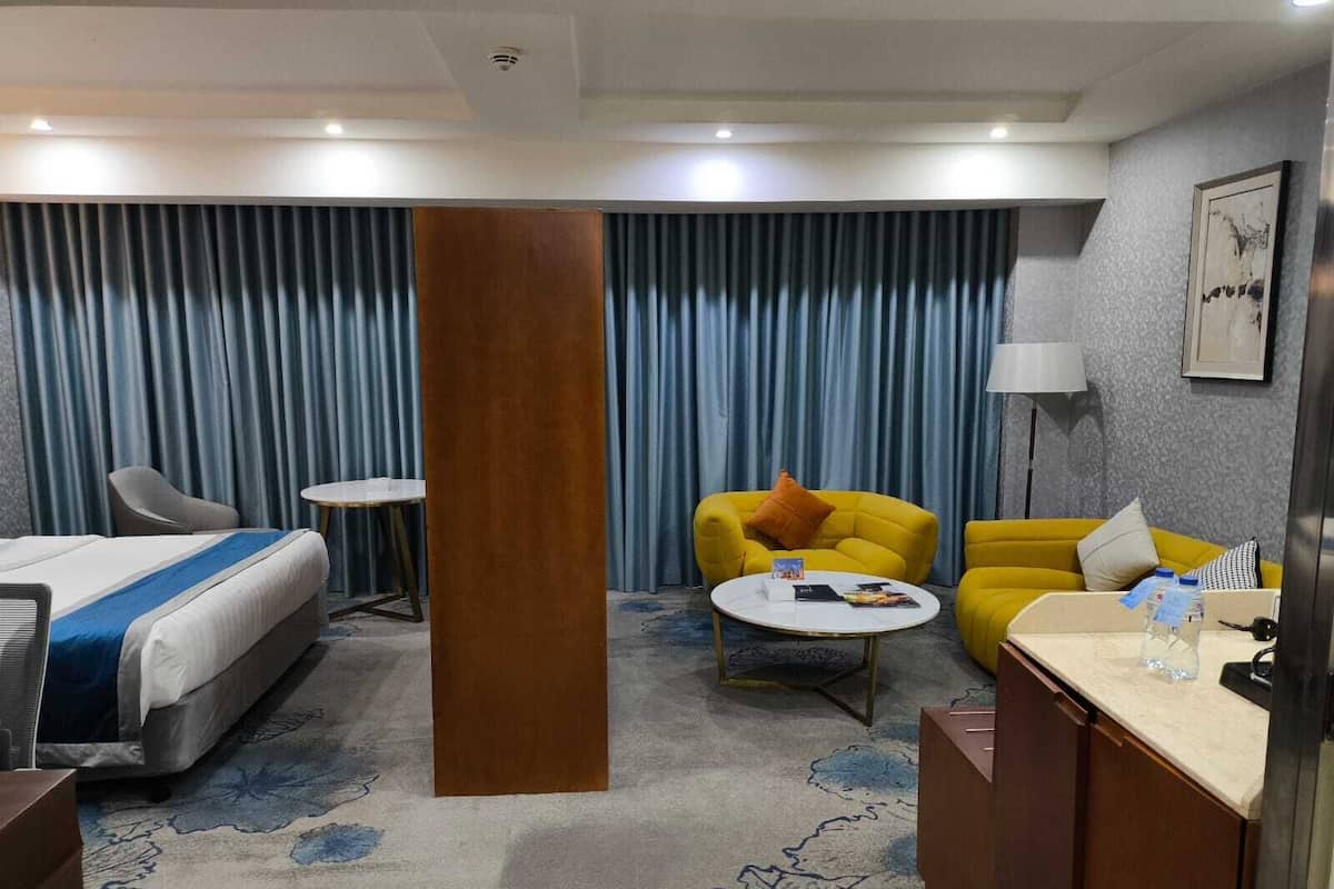 Quarto de hotel com cama, escrivaninha, cadeira, sofá e mesa de centro.