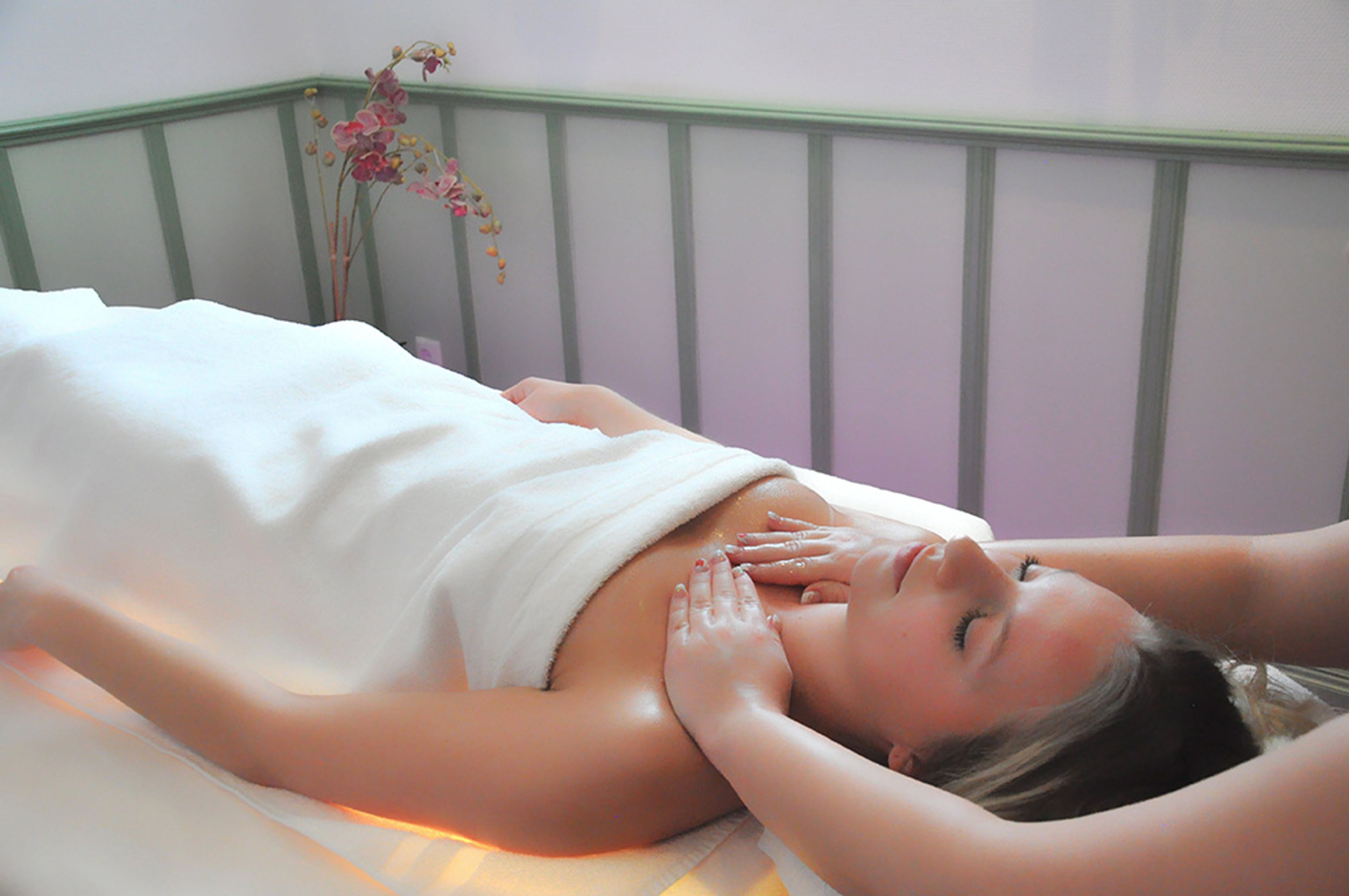 A person receiving a massage in a room with a green-framed bed and a wall-mounted flower arrangement.