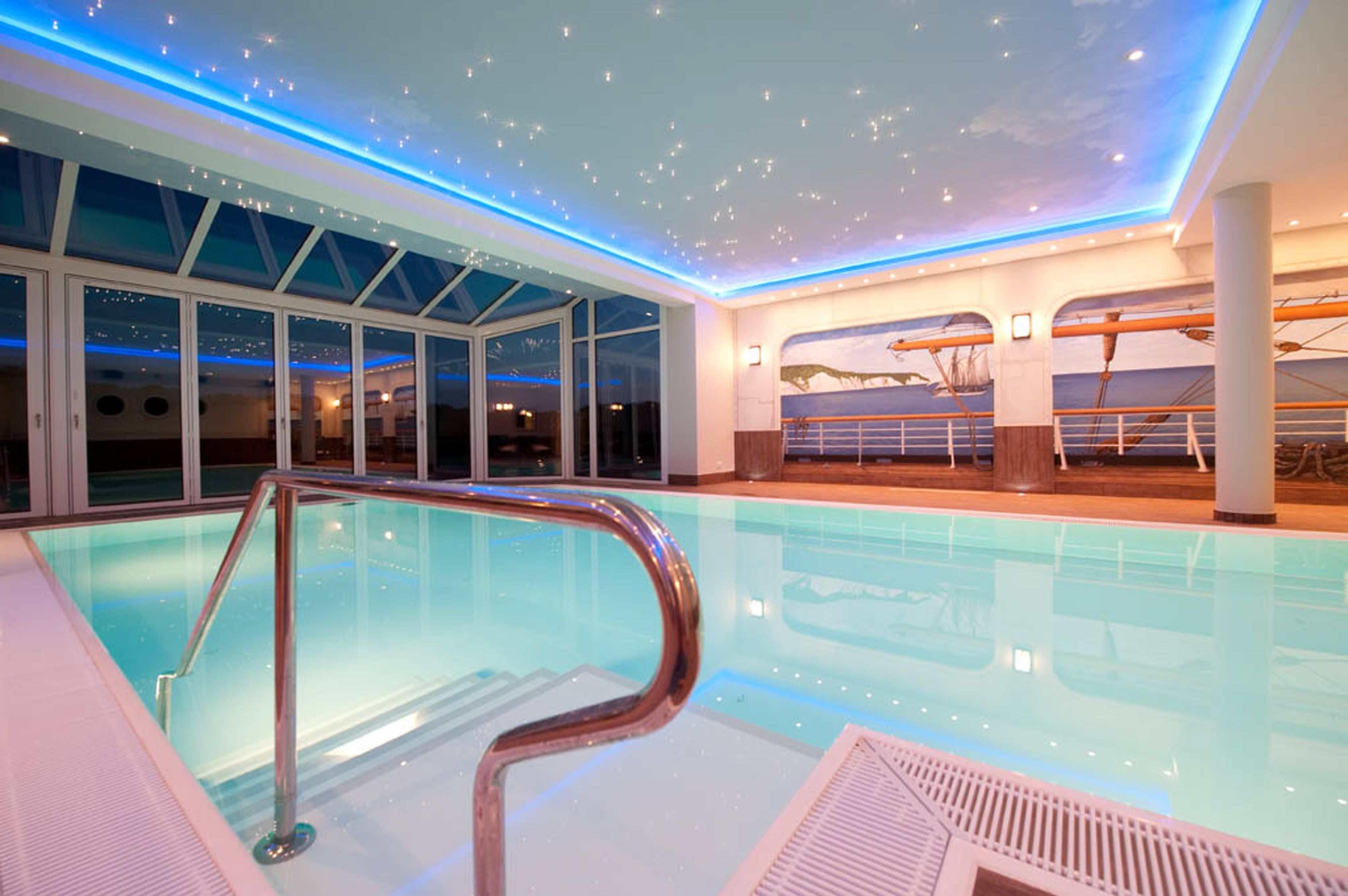 An indoor swimming pool with clear glass walls, a metal pool ladder, and a ceiling with a starry light design.