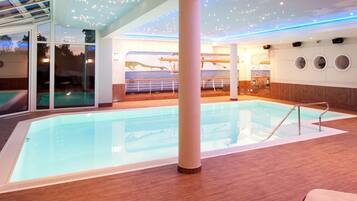 Relax by the pool in a serene indoor oasis with a rectangular pool, lounge chairs, and ambient lighting.