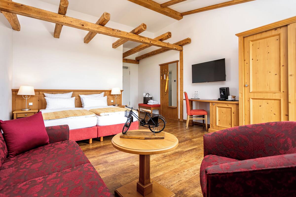 A room with a bed, a wooden table, a sofa, a bicycle, and a TV.