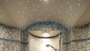 Une douche carrelée au design incurvé, une pomme de douche fixée au mur et une petite poubelle.